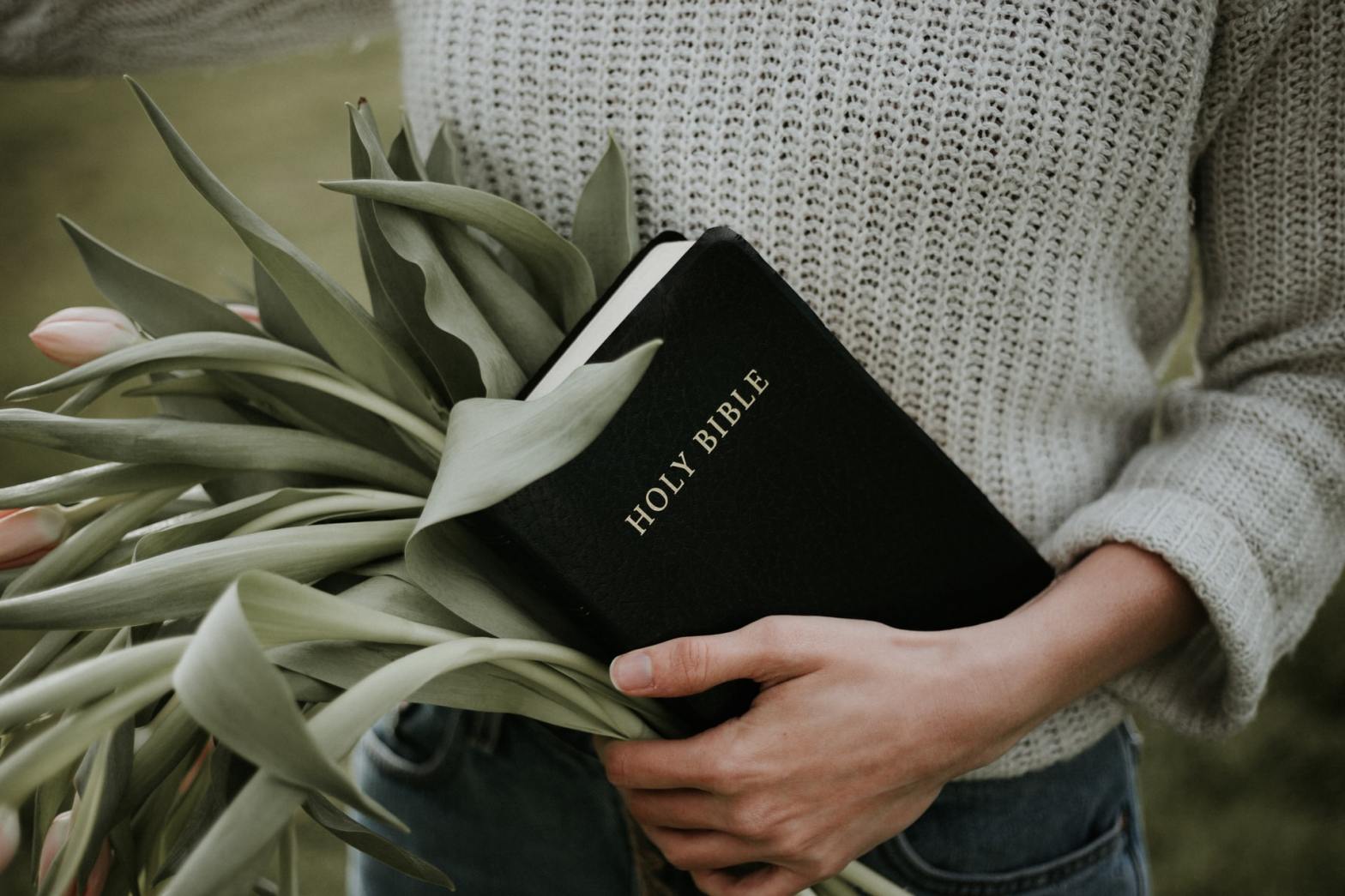 A person holding the Bible and a bunch of tulips