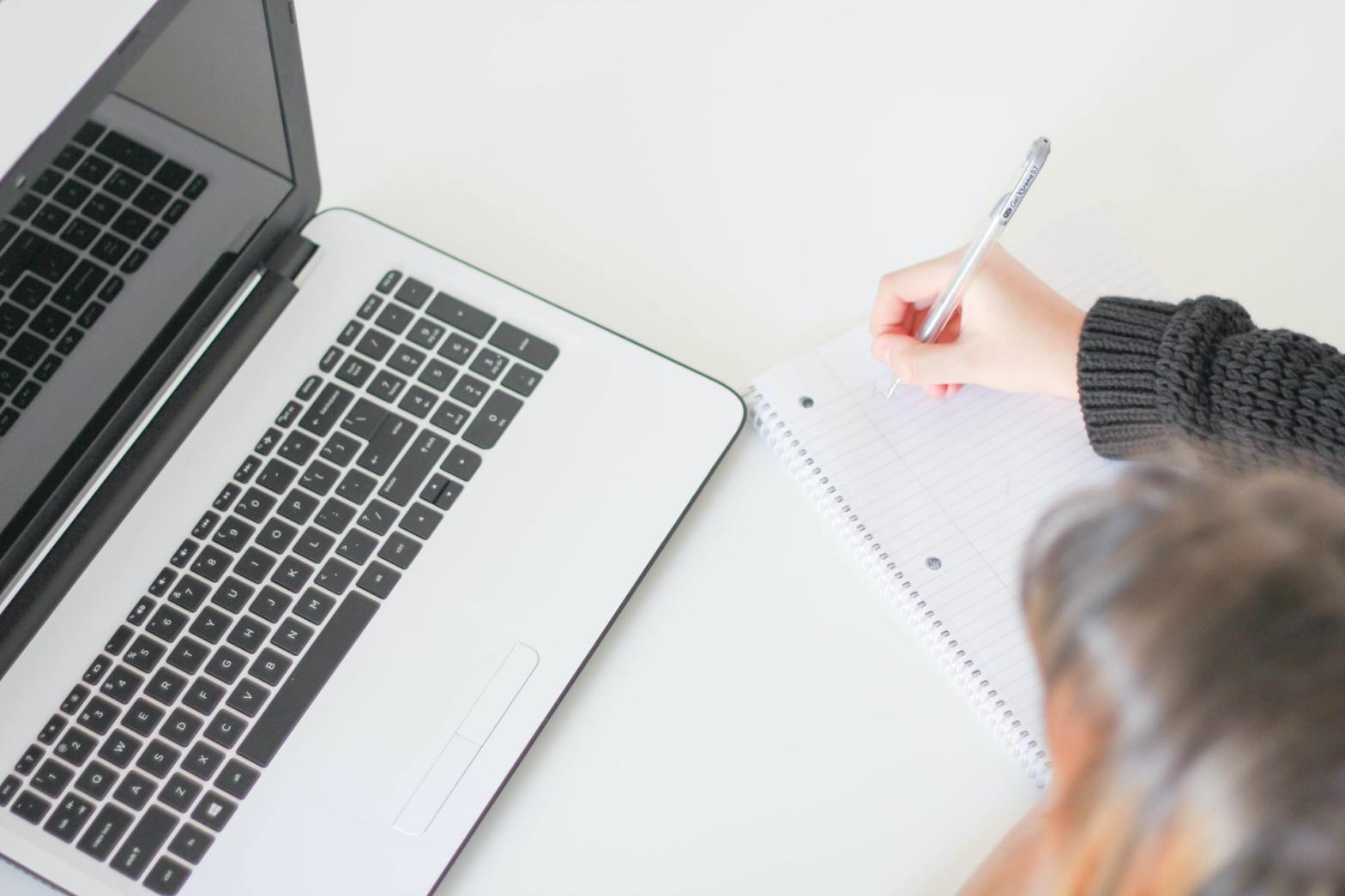 A girl writing in front of a laptop